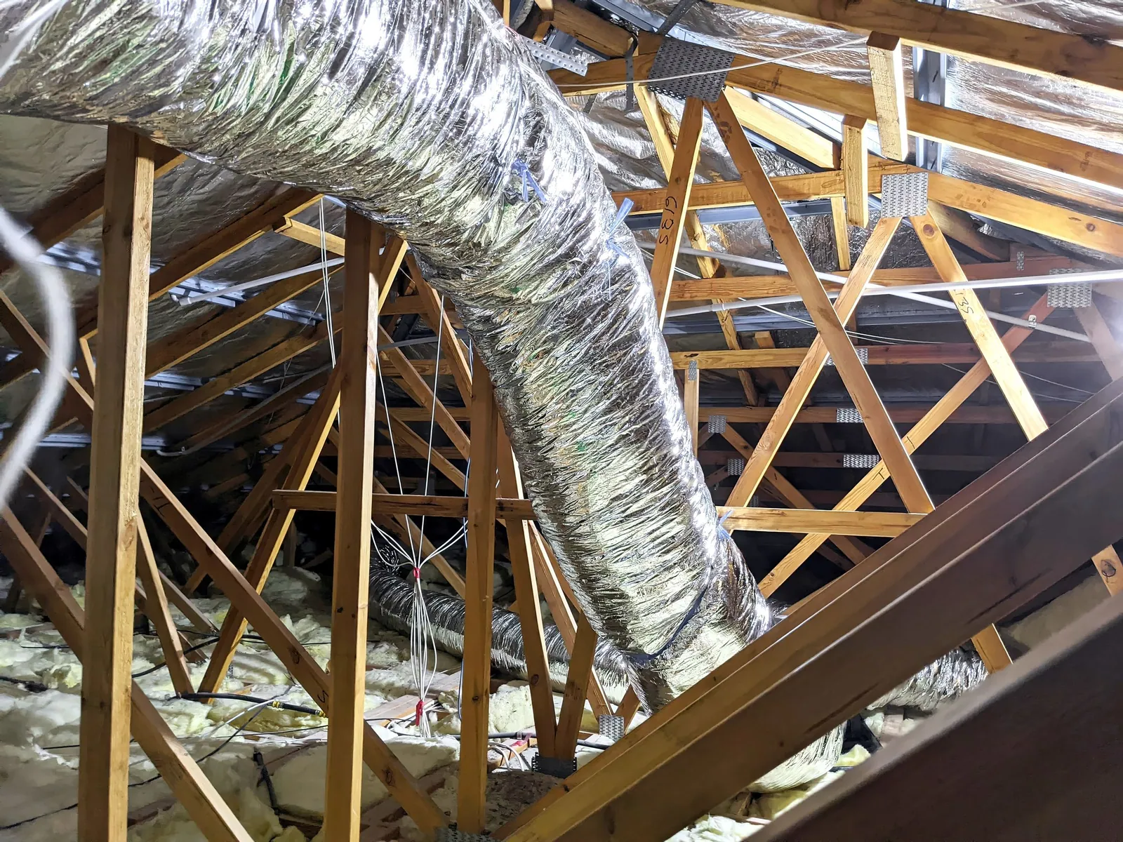 Insulated flexible ductwork running between roof trusses in a roof cavity