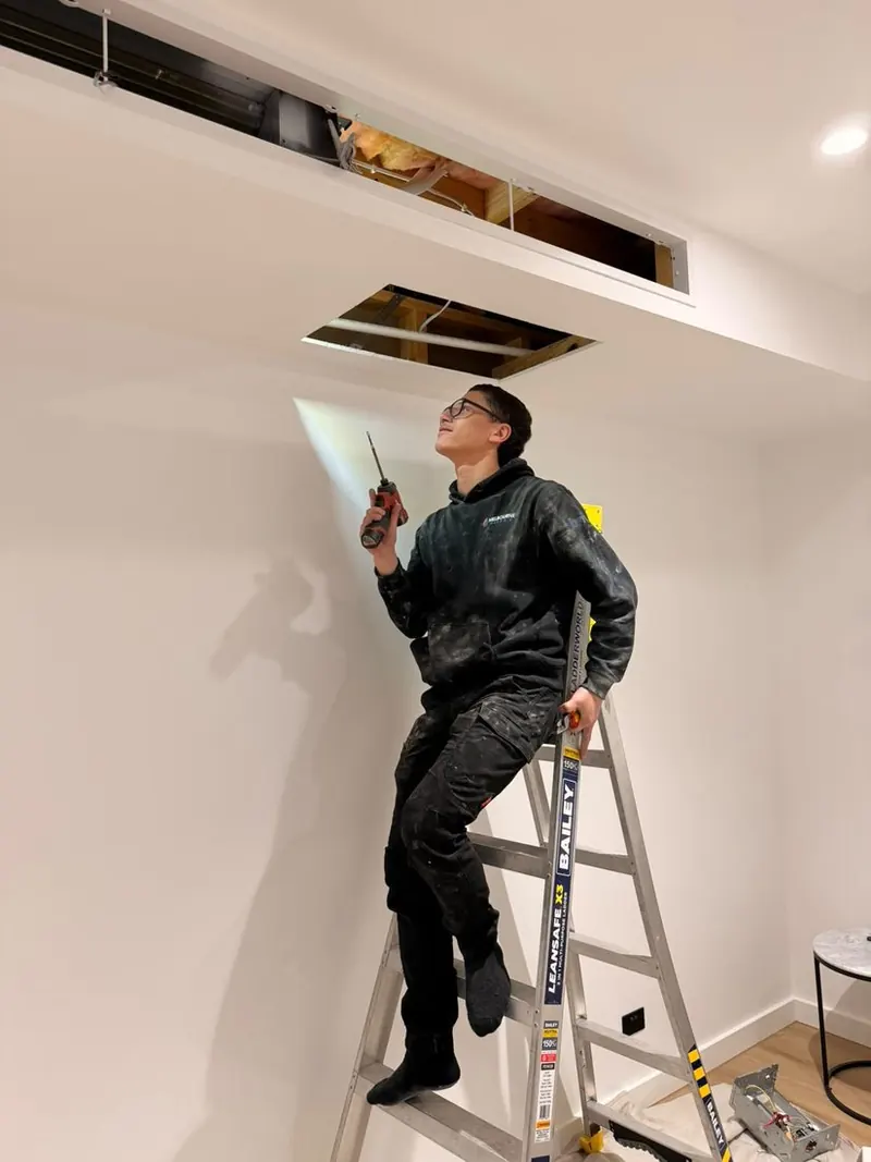 A Macedon Ranges Gas & Air technician on a ladder working at a ceiling access hatch during a ducted installation
